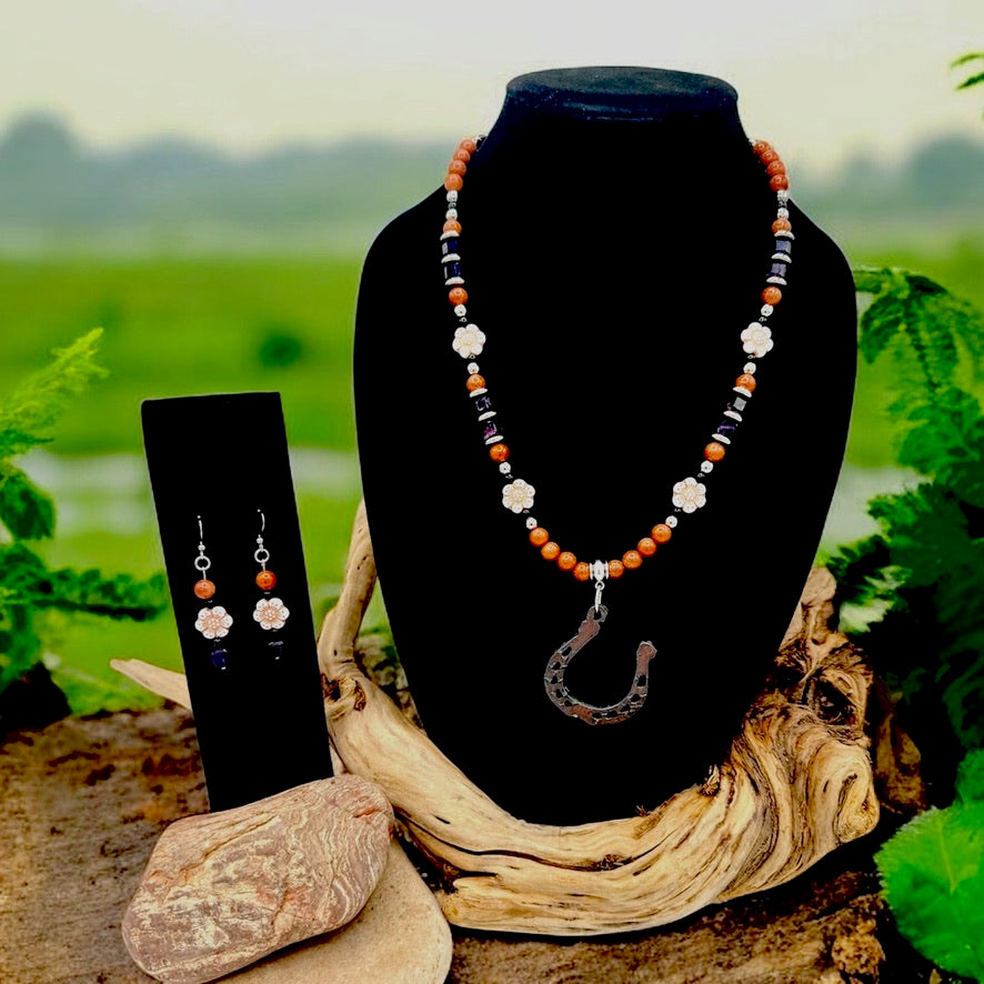 Copper goldstone beaded necklace with flower accents and a horseshoe pendant, displayed with matching drop earrings on a black bust.