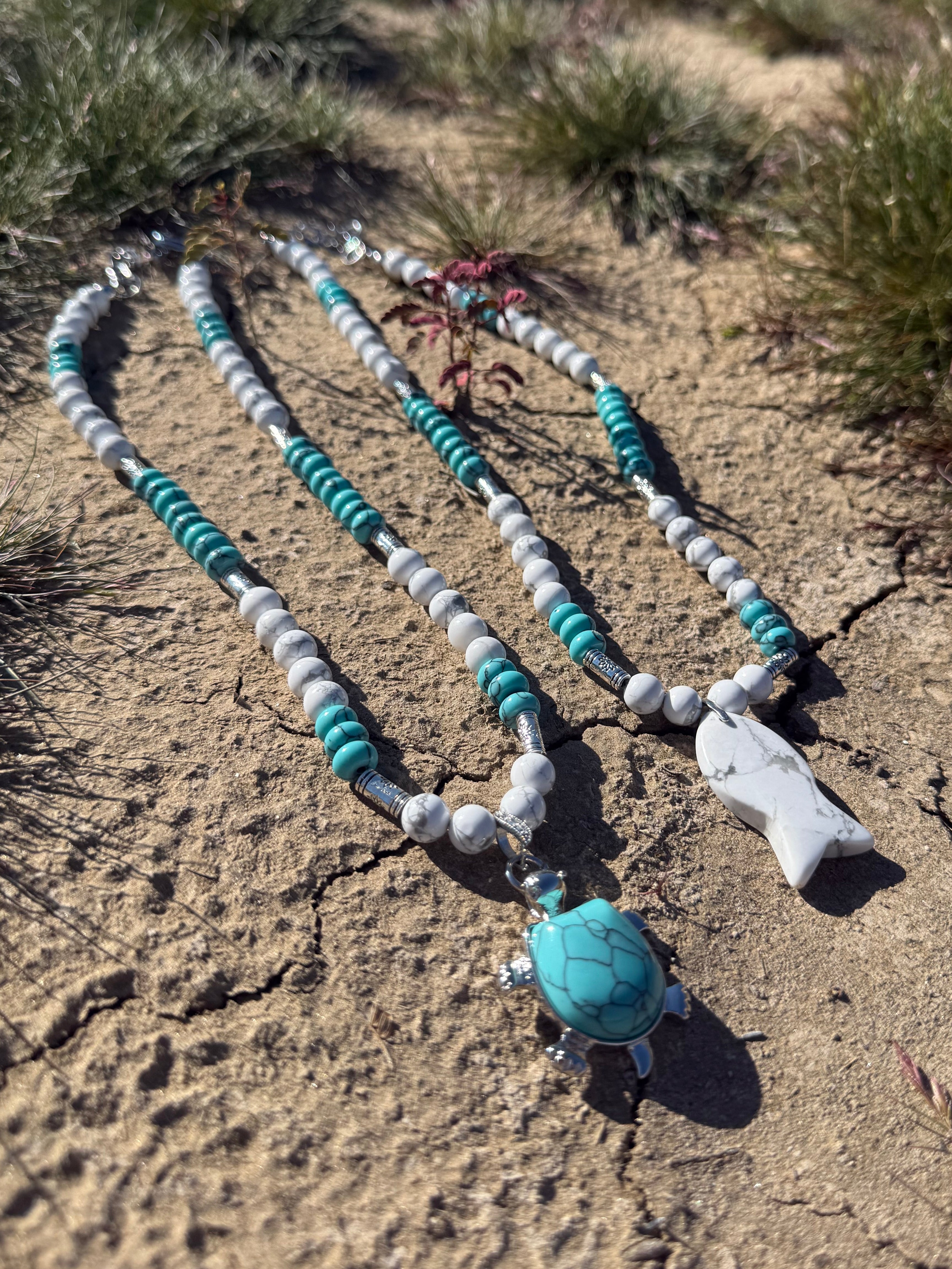 Necklace with turquoise and white beads on a sandy surface
